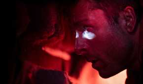 Ben Richards (Glen Powell), in a dim, red-lit car trunk, peers through a bullet hole to the outside in the 2025 adaptation of Stephen King's The Running Man