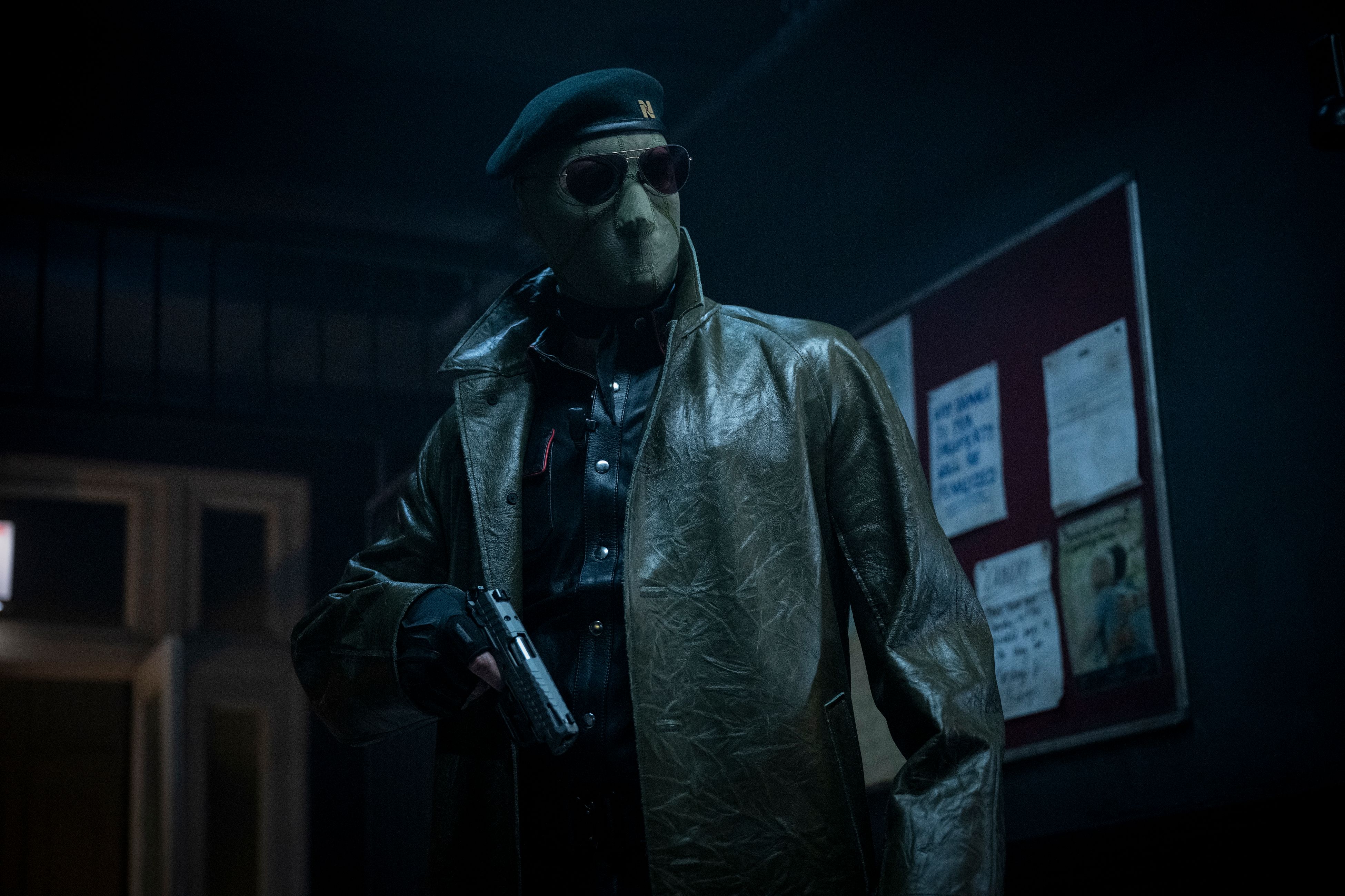 Lee Pace (though you can't tell it's him, or anyone really) wears an ICE-style face mask, sunglasses, and leather jacket and holds a gun in the 2025 Running Man