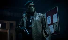 Lee Pace (though you can't tell it's him, or anyone really) wears an ICE-style face mask, sunglasses, and leather jacket and holds a gun in the 2025 Running Man