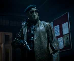 Lee Pace (though you can't tell it's him, or anyone really) wears an ICE-style face mask, sunglasses, and leather jacket and holds a gun in the 2025 Running Man