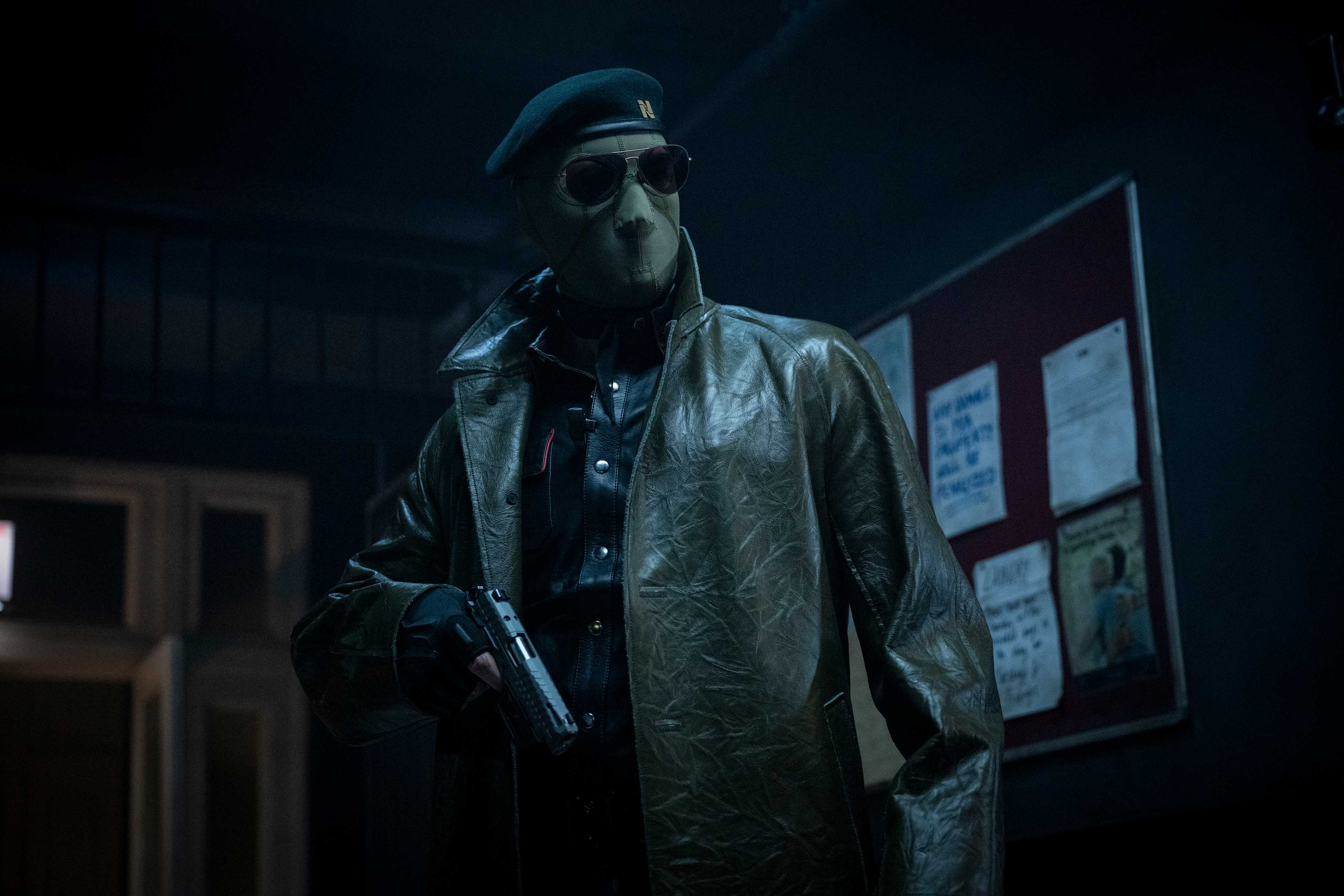 Lee Pace (though you can't tell it's him, or anyone really) wears an ICE-style face mask, sunglasses, and leather jacket and holds a gun in the 2025 Running Man