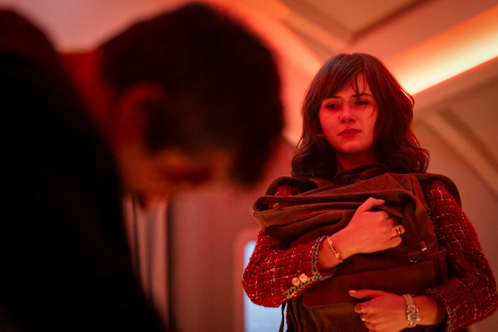 Ben Richards (Glen Powell) slumps in his seat on a red-lit plane, his back to the camera, while Amelia (Emilia Jones) clutches a parachute and looks worried in the 2025 Running Man