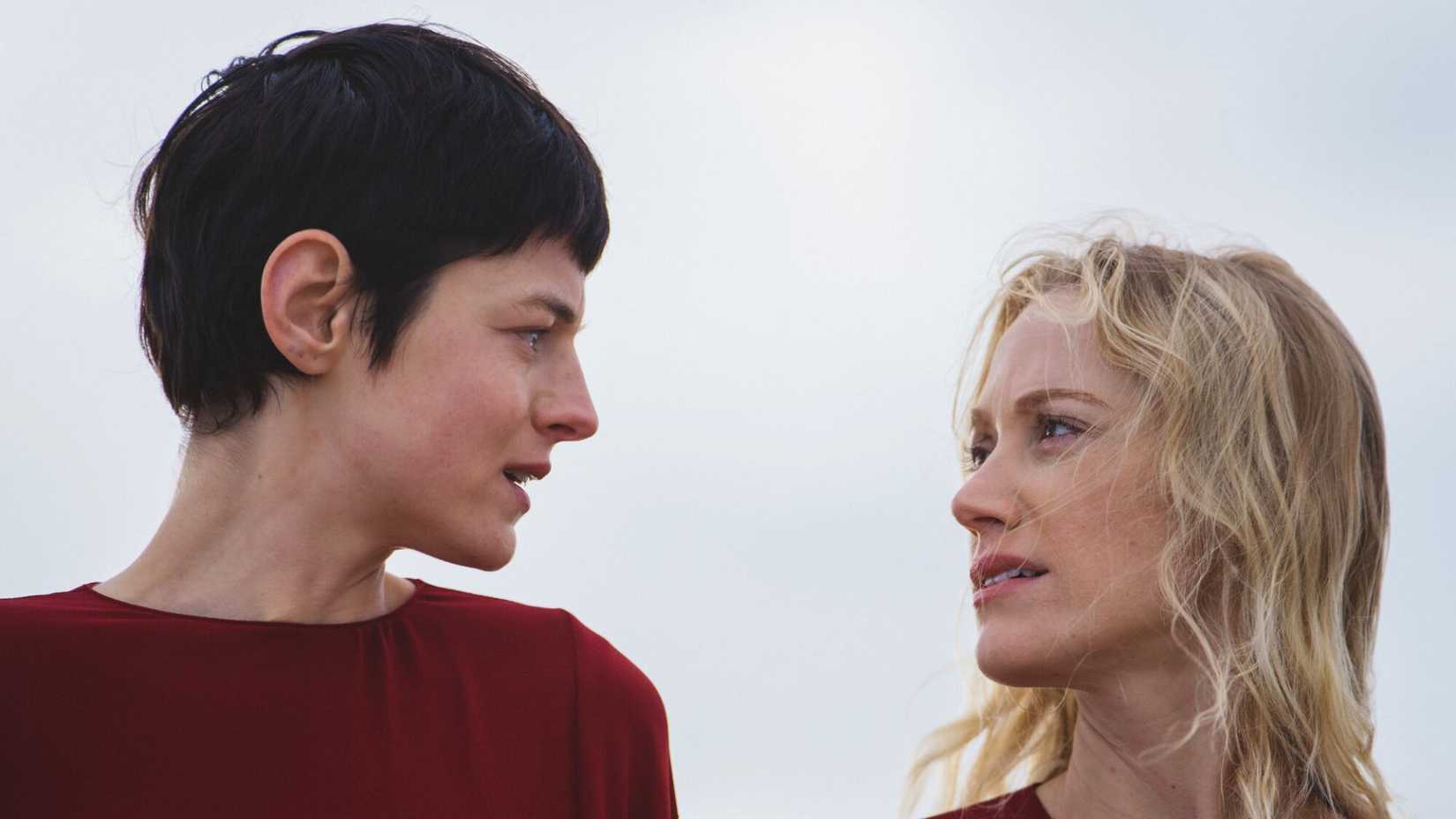 Emma Corrin as Hero and Maika Monroe as Cherry face each other, both in red against a white backdrop.
