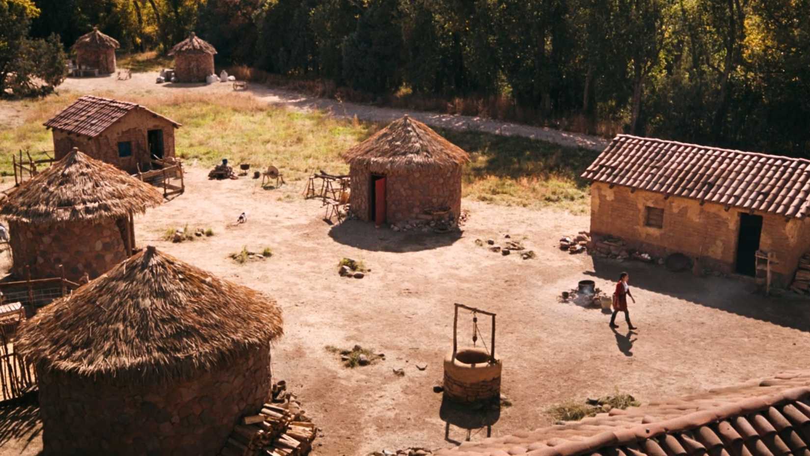 An image from Pluribus finale. It shows an abandoned village with a young woman walking away, a small goat trailing after her.