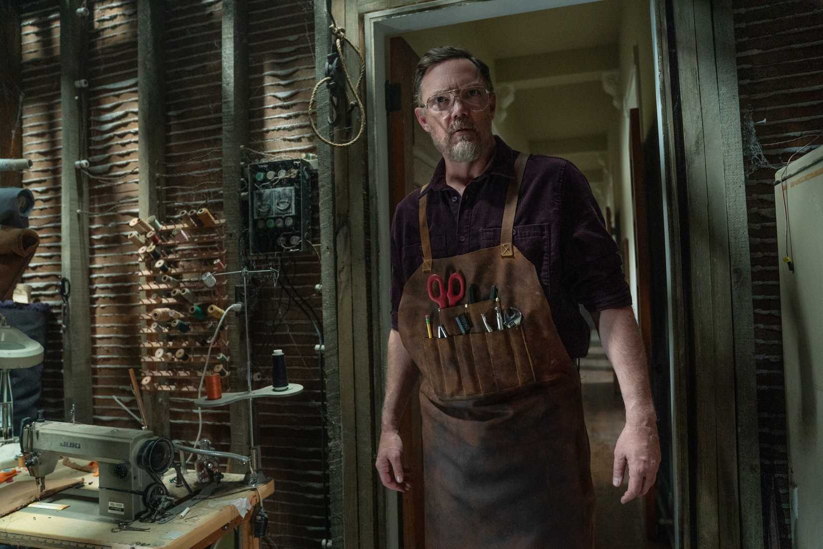 Matthew Lillard in Five Nights at Freddy's 2, standing in a doorway wearing a leather apron packed with tools