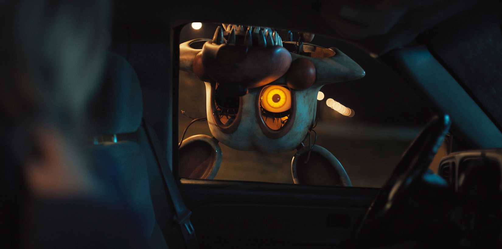An upside-down animatronic with a missing eye and sharp, pointed teeth hangs outside of a car window in Five Nights at Freddy's 2