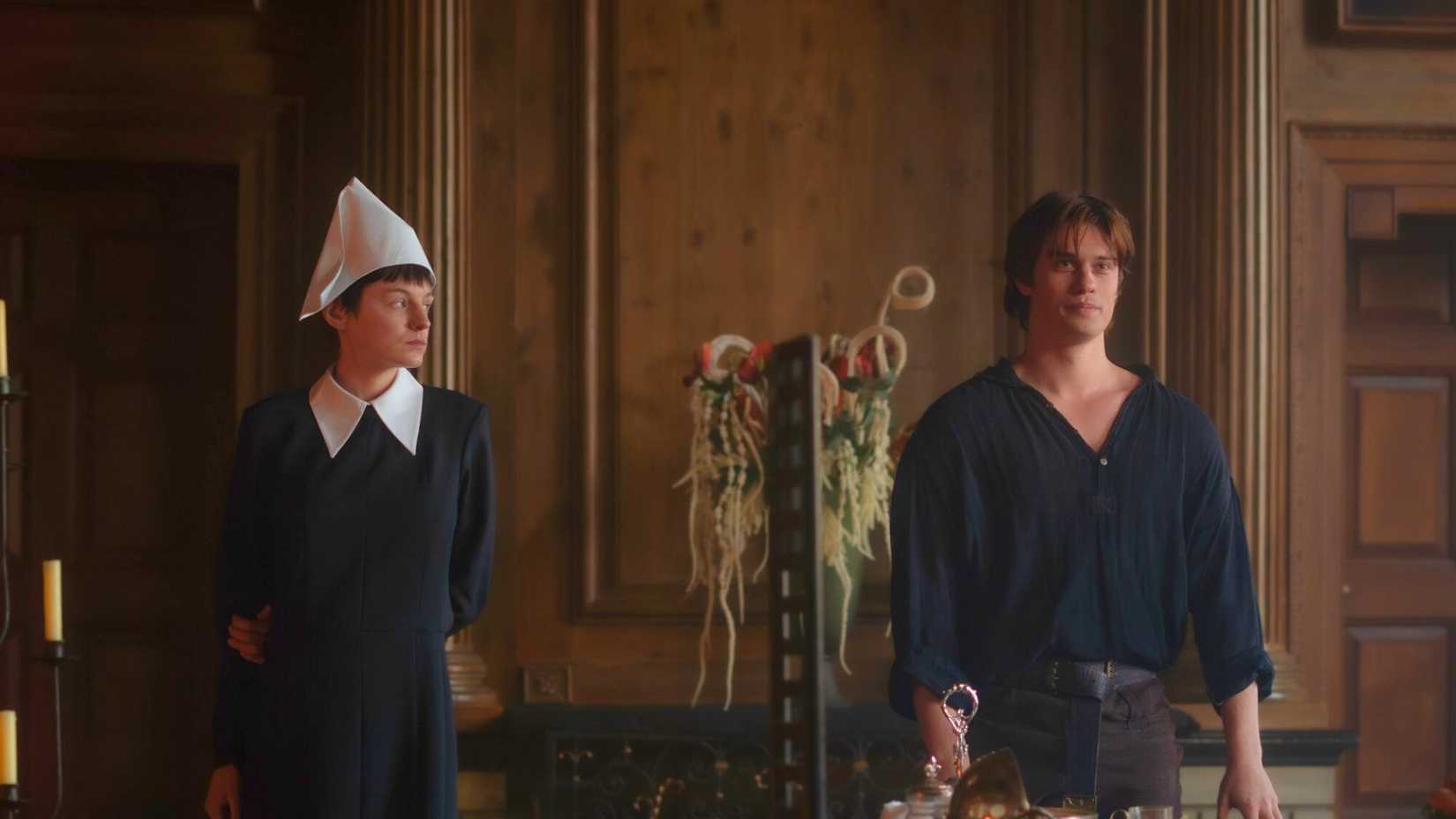 Emma Corrin and Nicholas Galitzine standing side by side; Corrin in a black dress with white collar, Galitzine in a dark shirt.