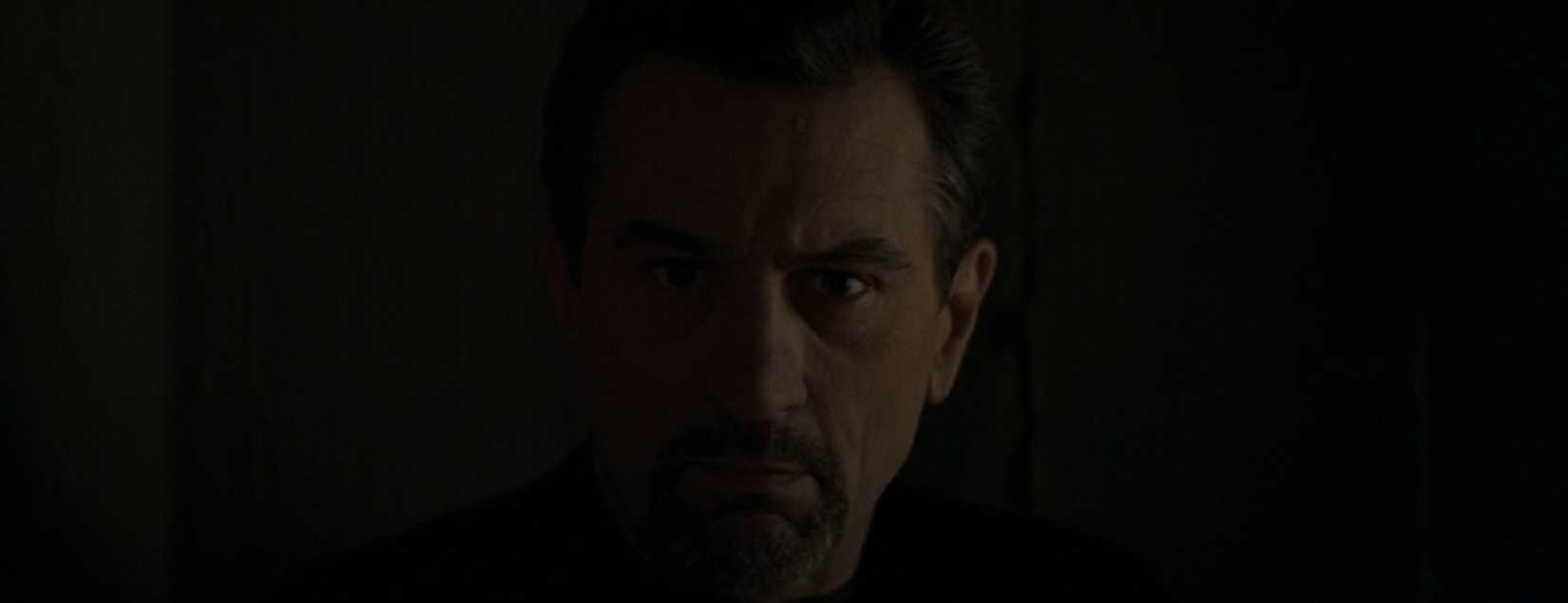 In a scene from the film Heat, Robert De Niro looks into the shadows in close-up, facing the camera and listening intently, aware that his team may be under surveillance.