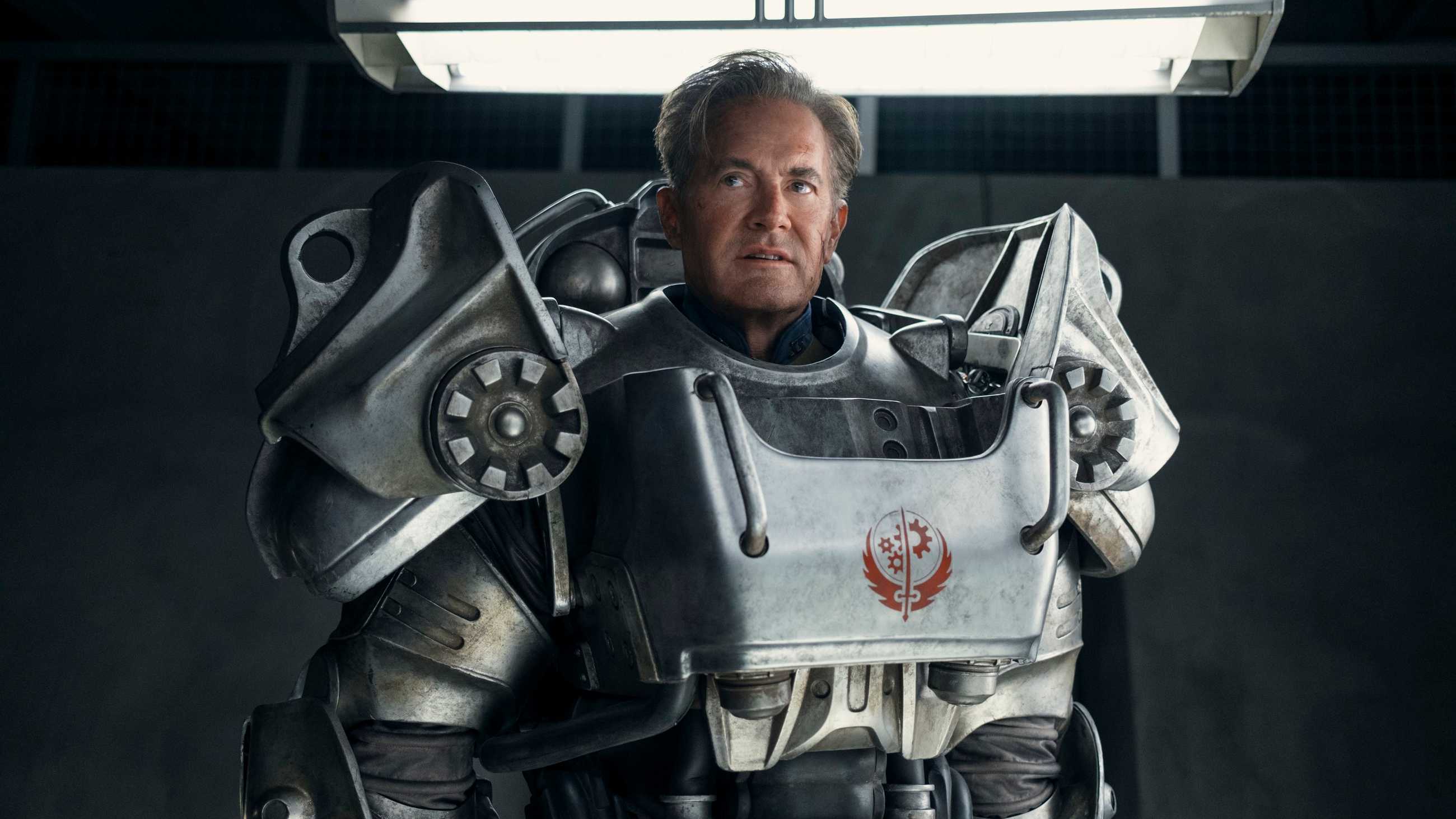 Hank MacLean (Kyle MacLachlan) se encuentra bajo luces fluorescentes con una servoarmadura de la Hermandad del Acero en la temporada 2 de Fallout.