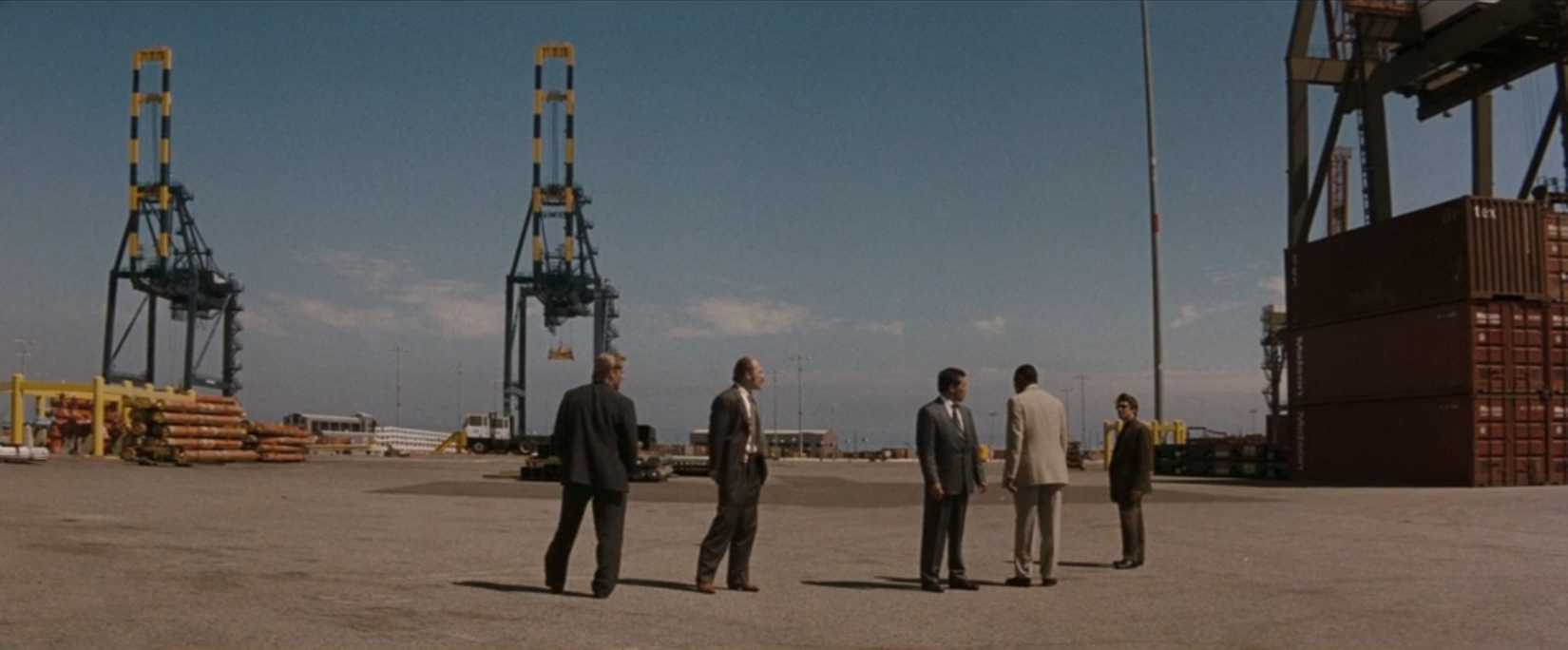In a scene from the film Heat, a group of police officers led by Vincent Hanna (Al Pacino) (seen in a wide shot) inspect an industrial area for signs of criminal activity.