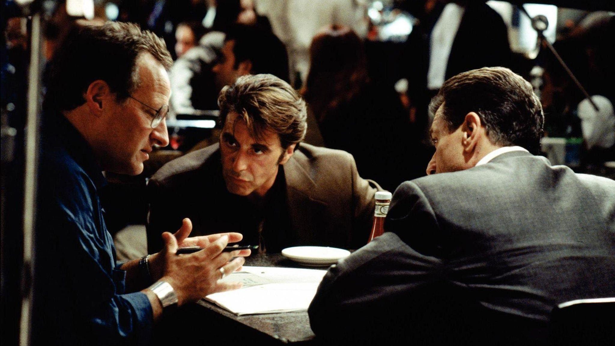 In a behind-the-scenes shot from the movie Heat, director Michael Mann consults with actors Al Pacino and Robert De Niro, during the filming of the famous diner scene where the two legendary performers sit down for a quiet cup of coffee.