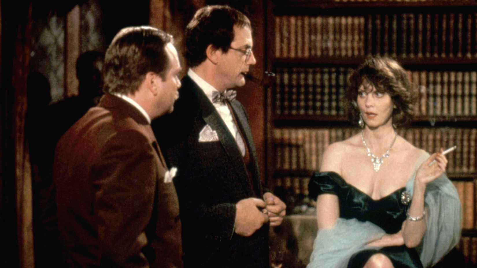 Miss Scarlet (Lesley Ann Warren) smokes a cigarette while being oggled by Professor Plum (Christopher Lloyd) and Colonel Mustard (Martin Mull)