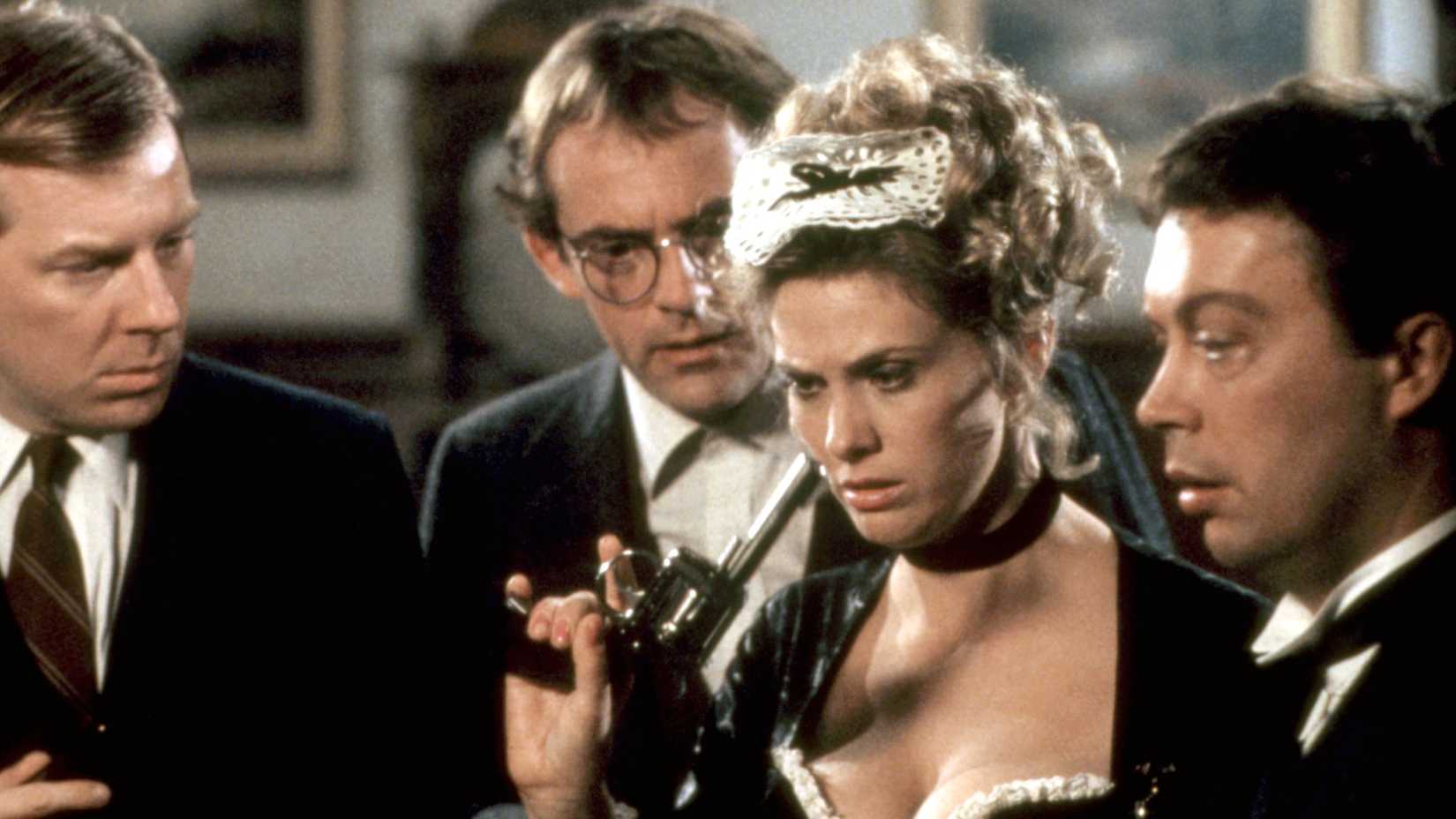 The French maid Yvette (Colleen Camp) holds a gun while surrounded by Mr. Green (Michael McKean), Professor Plum (Christopher Lloyd) and Wadsworth (Tim Curry)
