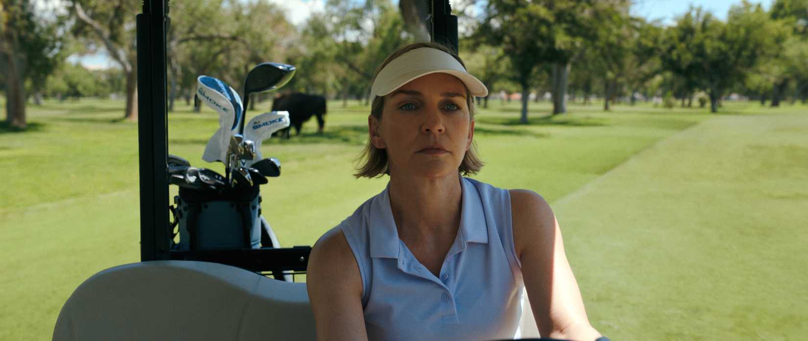 Carol Sturka (Rhea Seehorn), in a white sleeveless polo and sun shade, drives a golf cart in Pluribus