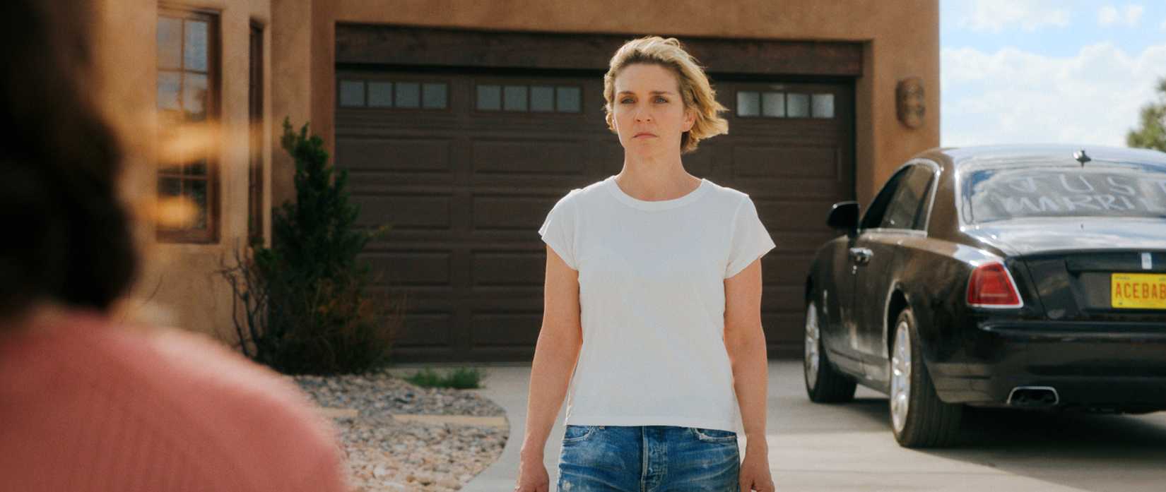 Carol (Rhea Seehorn) stands in her driveway, looking stricken, as Zosia (Karolina Wydra) approaches in Pluribus