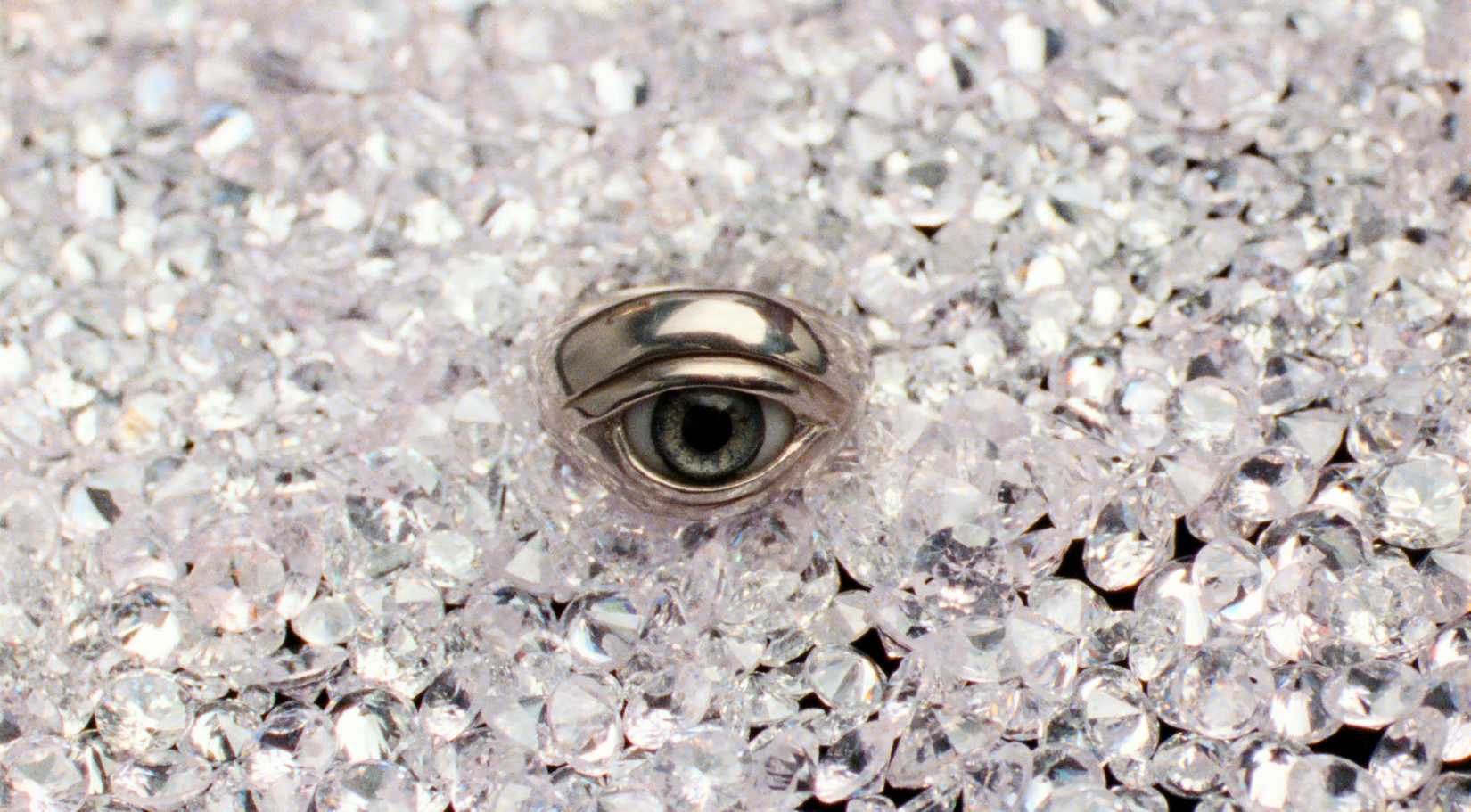 A ring with an inset glass eye lies in a bed of sparkling white diamonds in Reflection in a Dead Diamond