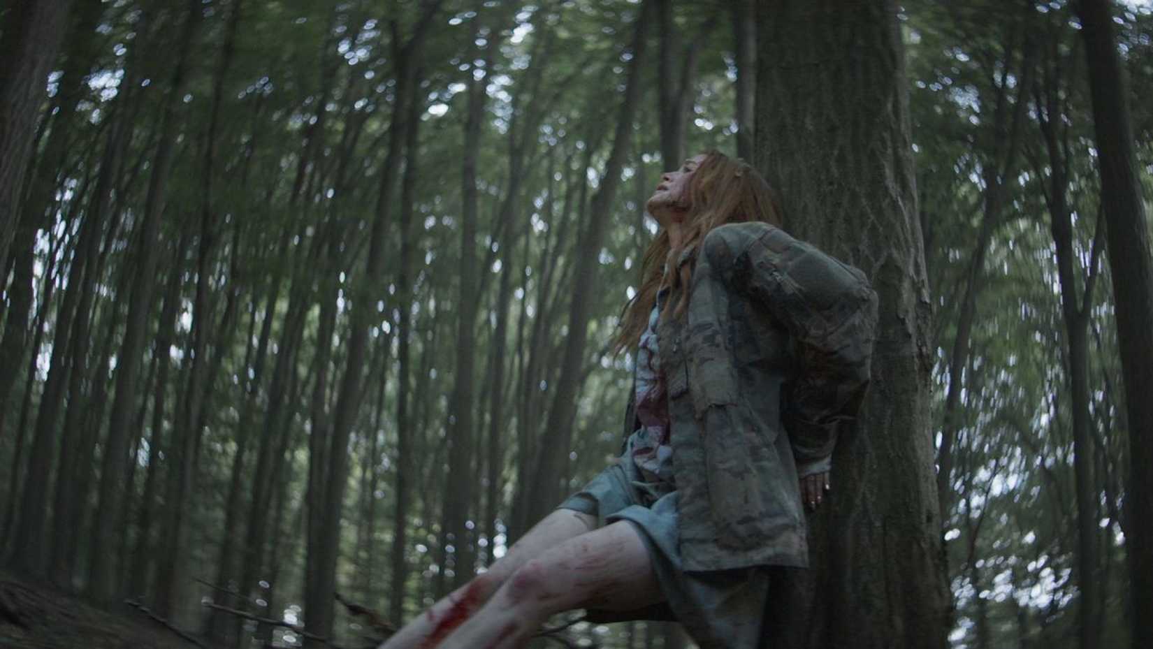 In a low-angle shot, Madelaine Petsch panics as her character is pursued through heavy woods in a scene from The Strangers: Chapter 2.