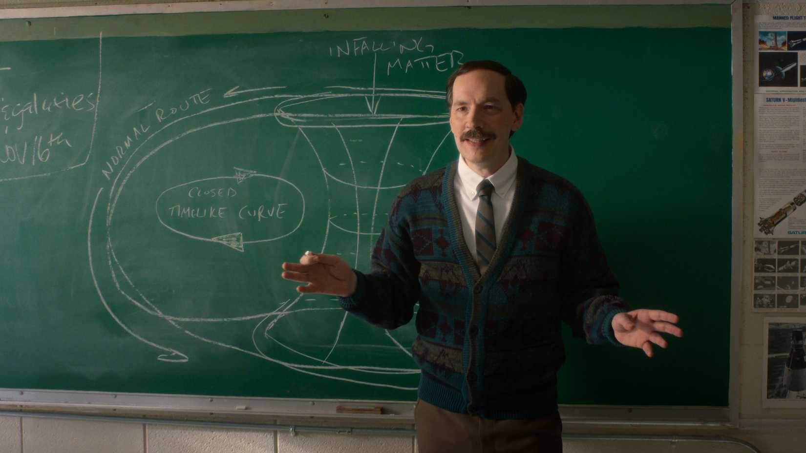 Hawkins Middle School science teacher Mr. Clarke (Randy Havens) teaches a lesson on wormholes in front of a green chalkboard in Stranger Things season 5