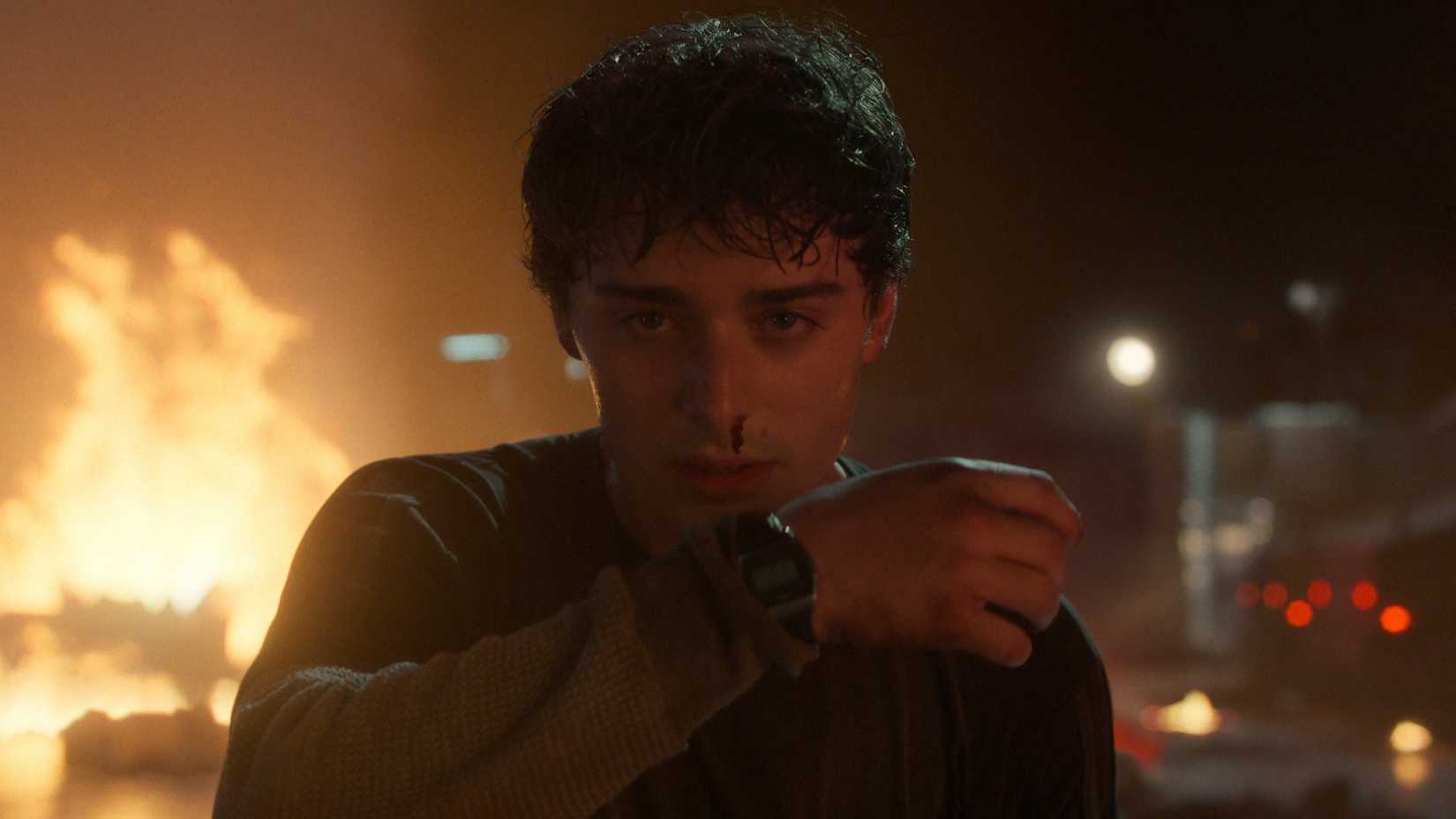 Will (Noah Schnapp) wipes away a nosebleed while a fire burns behind him after unleashing his powers in Stranger Things season 5, episode 4