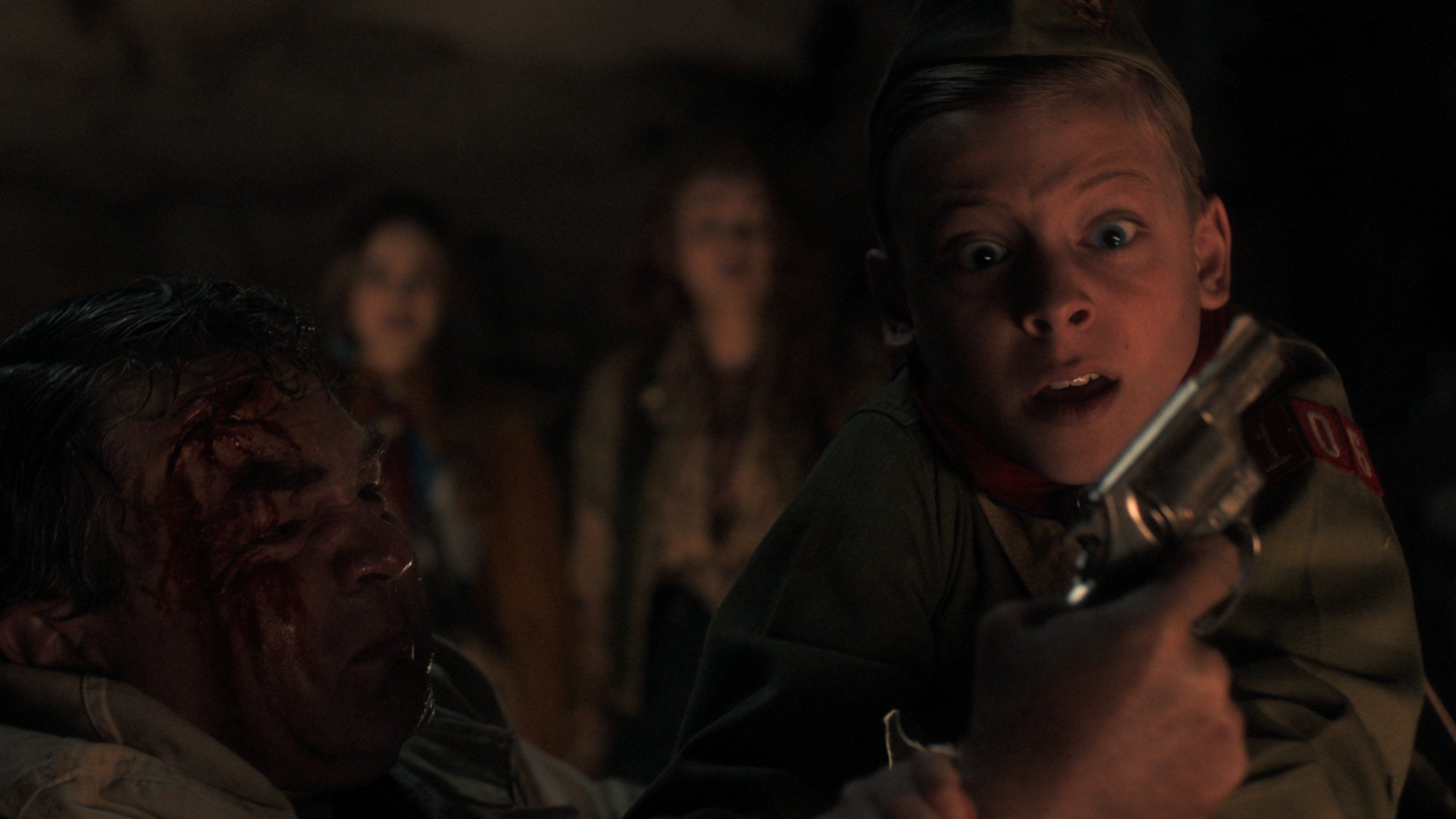 Holly Wheeler (Nell Fisher) and Max Mayfield (Sadie Sink) watch a young Henry Creel (Maksim Blatt) wrestle a man with a gun in Stranger Things season 5 episode 6