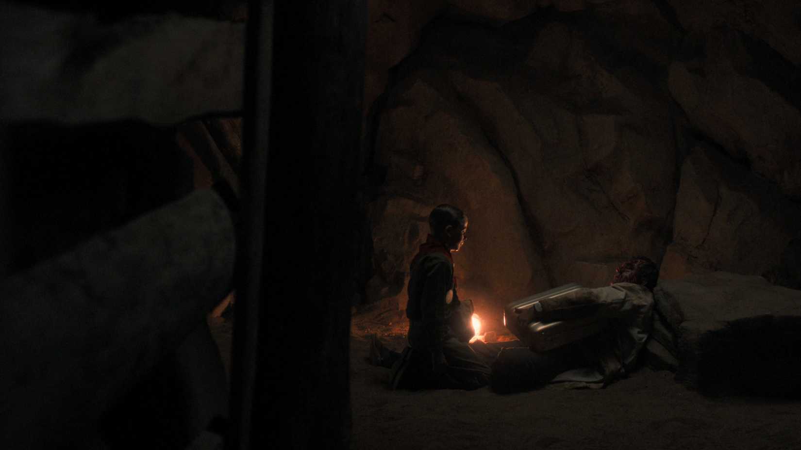A young Henry Creel (Maksim Blatt) kneels in front of a dead man holding a briefcase in a mineshaft in Nevada in Stranger Things season 5, episode 6