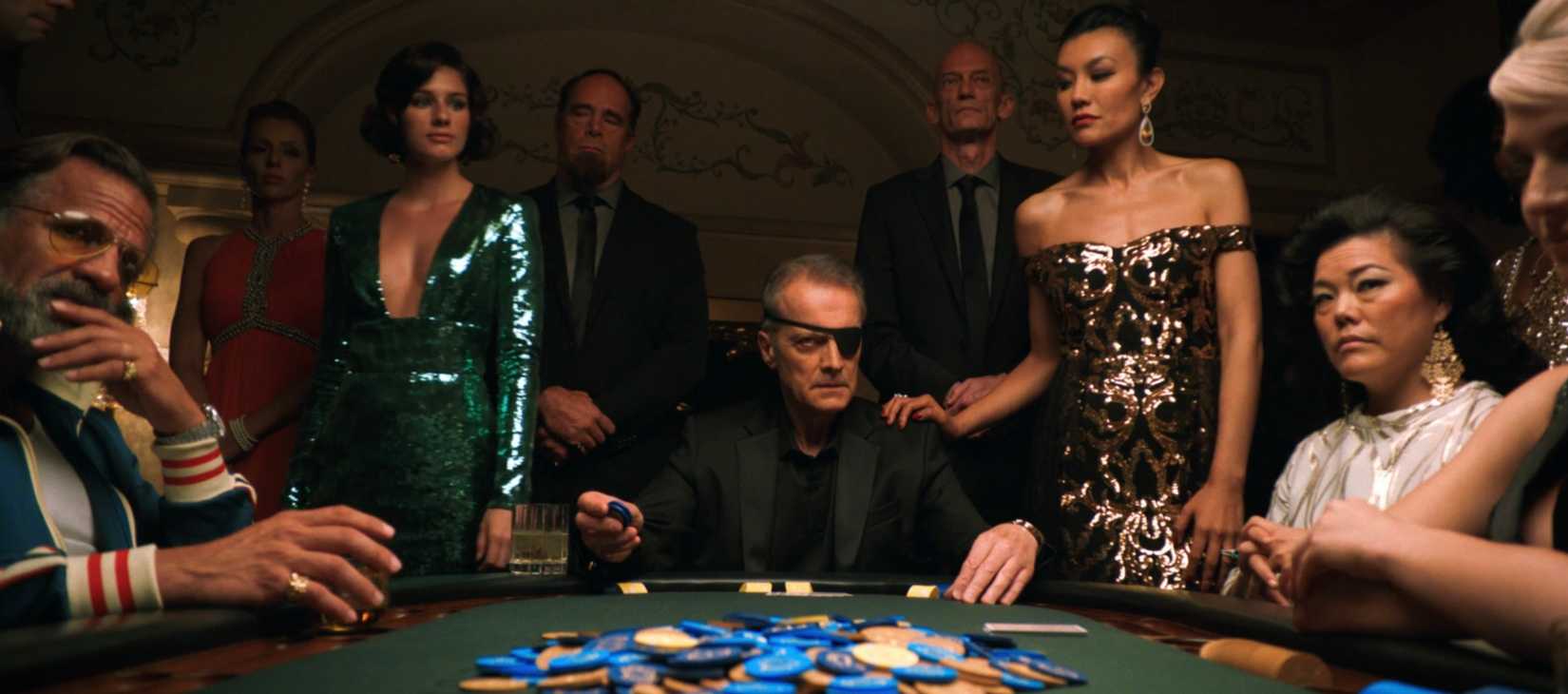 A stern-looking man in an eyepatch sits at a Vegas poker table, surrounded by serious-faced onlookers, in Pluribus episode 6
