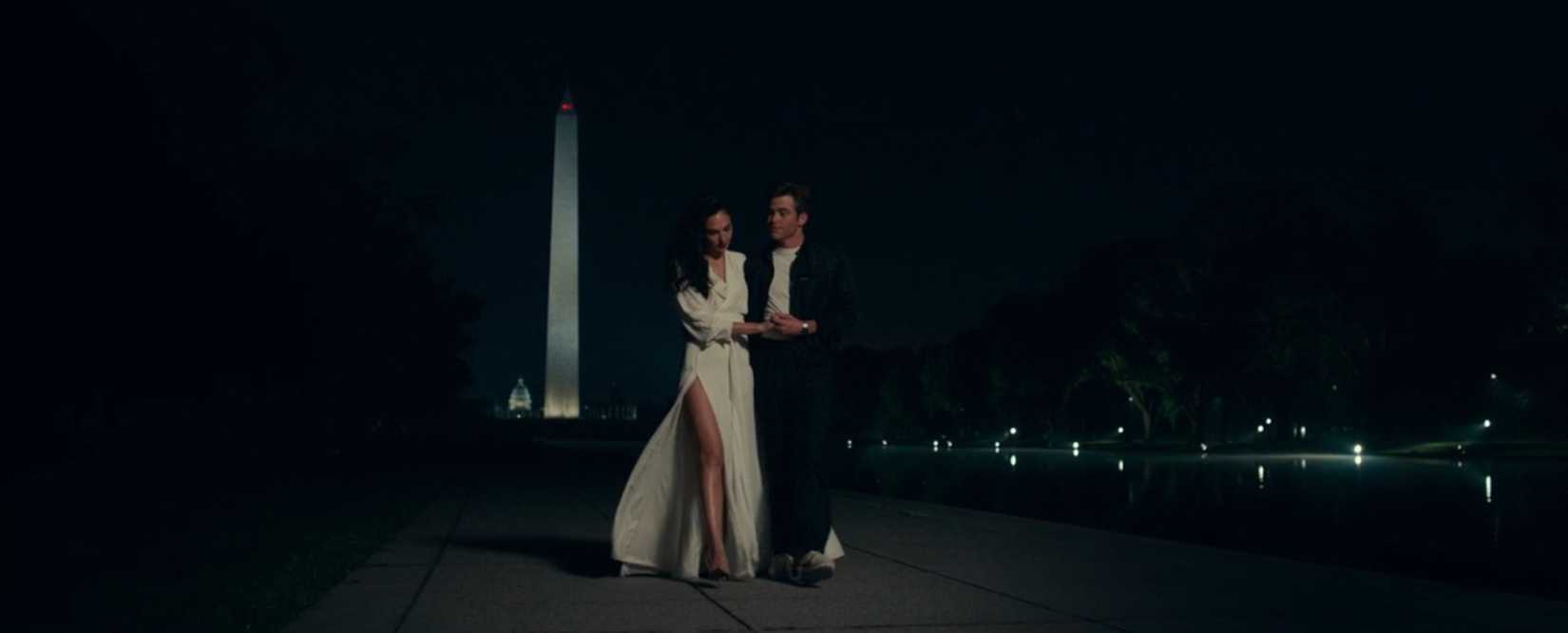 In a scene from Wonder Woman 1984, Diana (Gal Gadot) and Steve Trevor (Chris Pine) walk together on the Washington, DC mall at night, with the Washington Monument in the distance