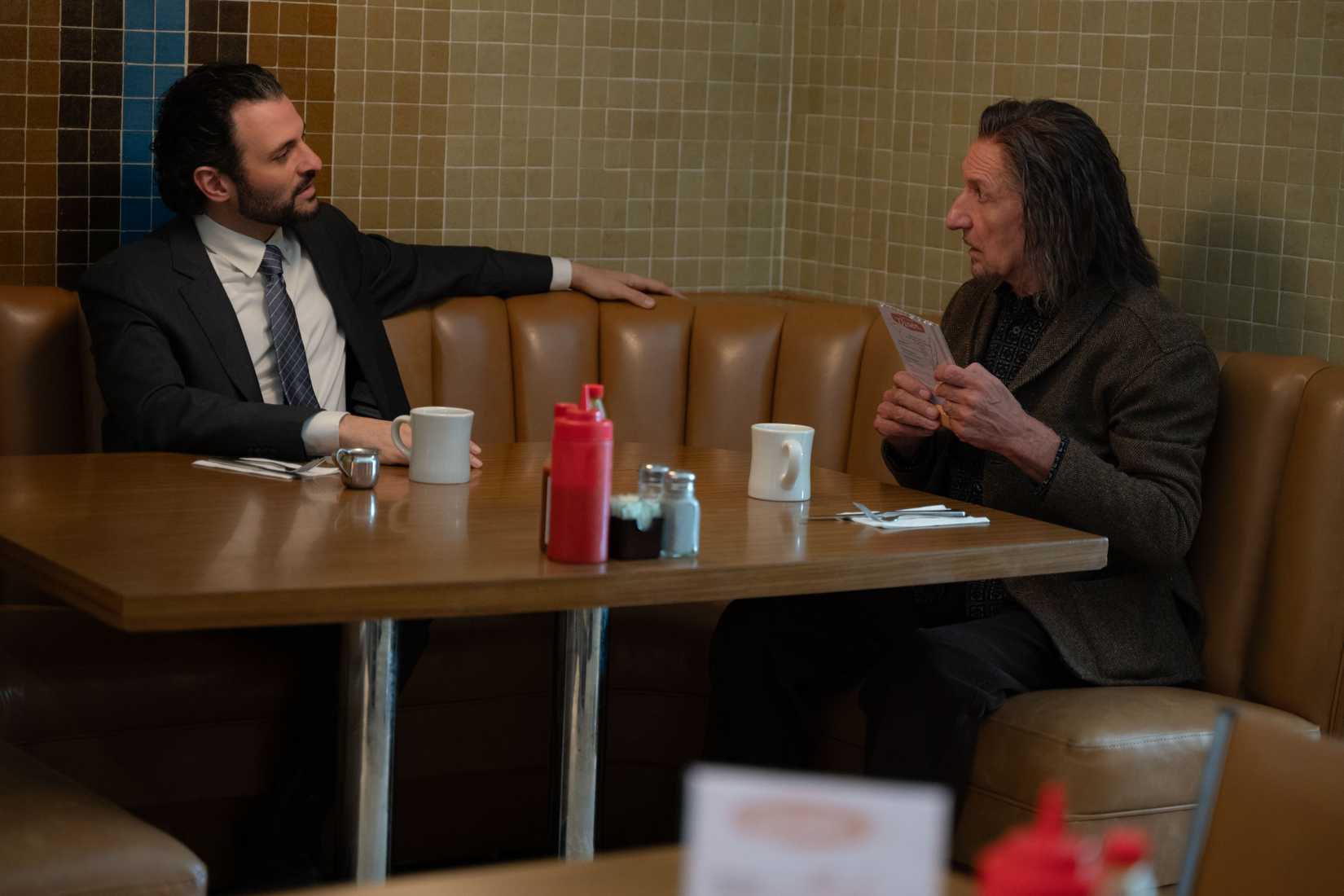Agent Cleary (Arian Moayed) sits in a diner booth with Trevor Slattery (Ben Kingsley) in Wonder Man