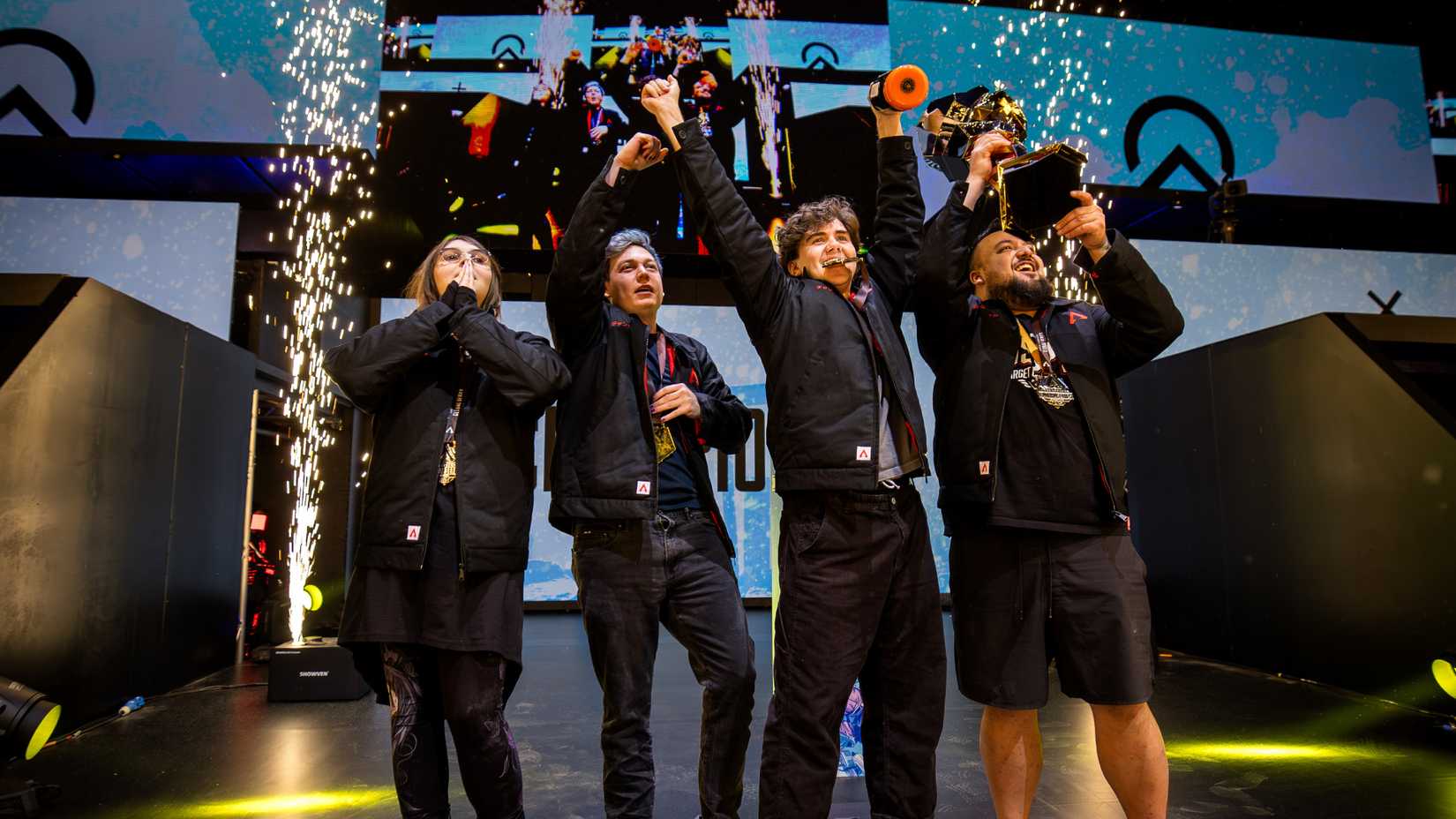 Team Oblivion holds up the ALGS Championship trophy as pyrotechnic sparks fly behind them.