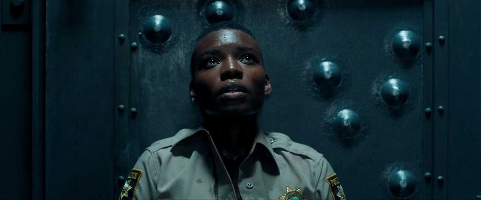 Alexis Louder braces herself against a bulletproof door in close-up in a tense scene from Copshop (2021)