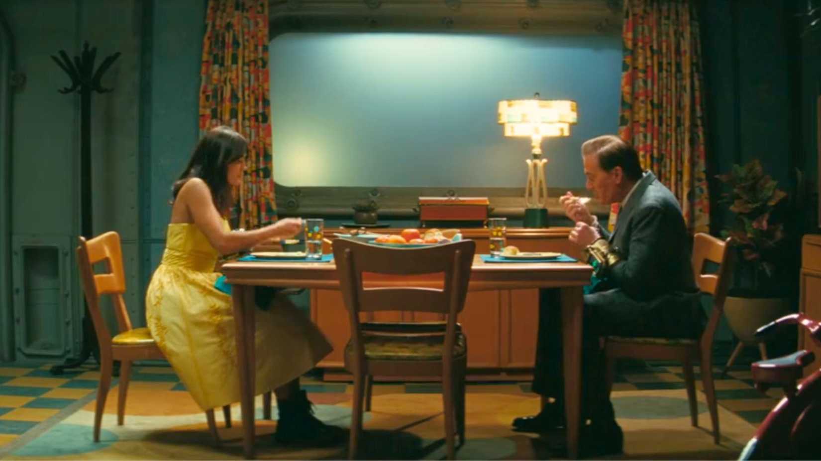 An image from Fallout season 2. It shows Lucy MacLean (Ella Purnell) in a yellow dress eating dinner. Across from her is her father, Hank MacLean, in a grey suit.