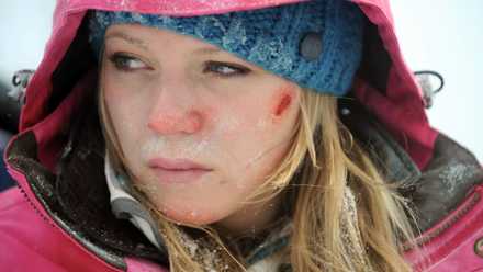 An image from Frozen 2010. Emma Bell as Parker O'Neal, blonde hair, a blue beanie, is covered in frostbite and looks uncomfortable.
