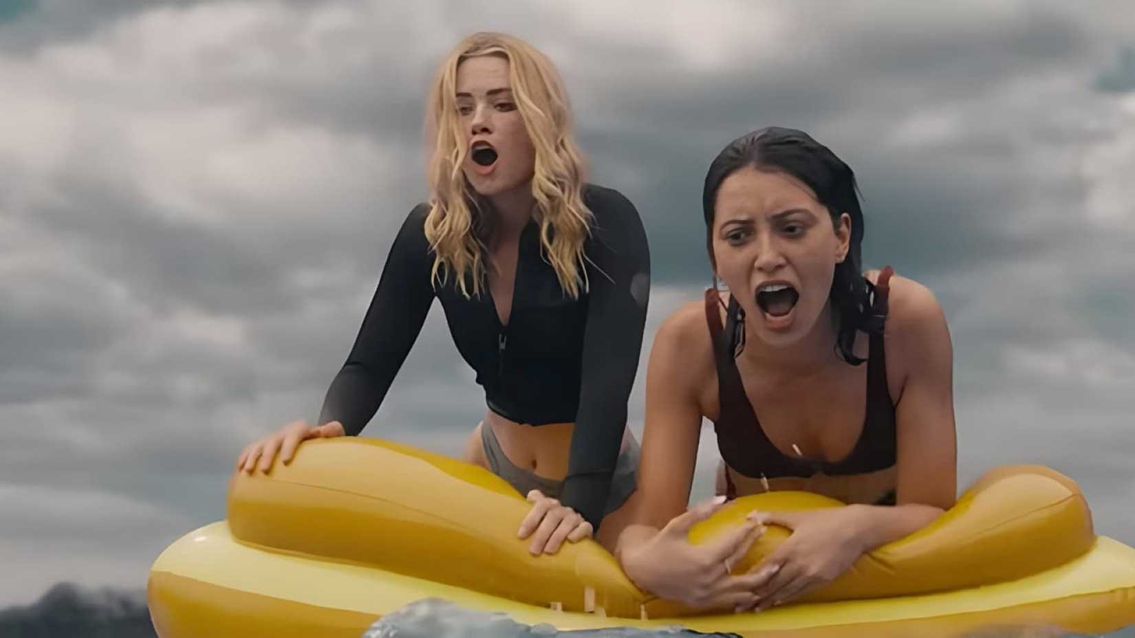 Two women stuck on a flimsy flotation device in the ocean call for help while nervously eyeing something in the water in a scene from Killer Whale.