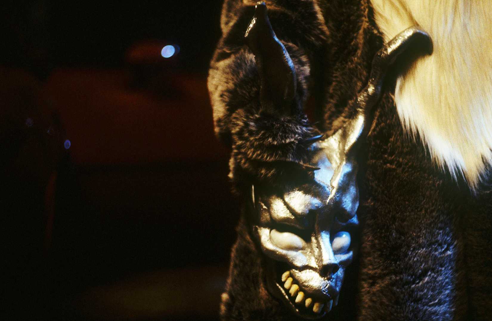 A clawed hand of a furry rabbit costume holds a distorted rabbit mask in Donnie Darko