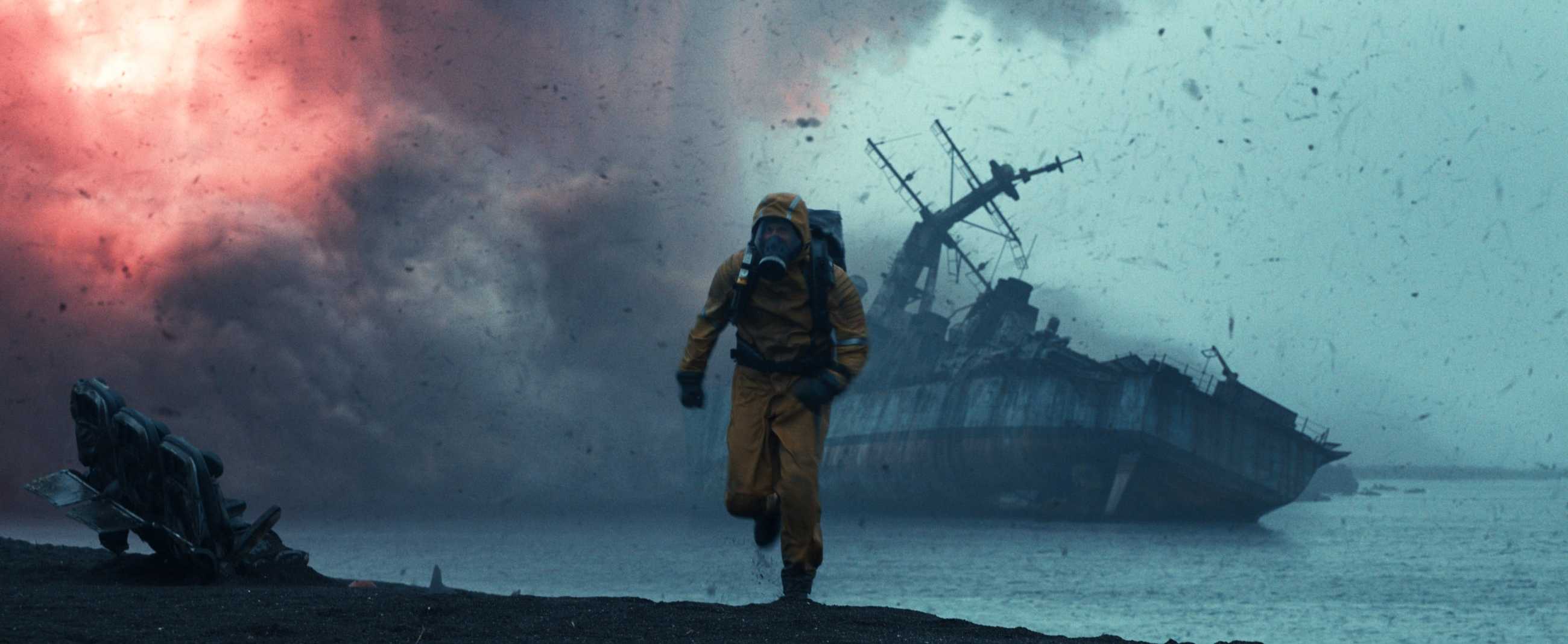 A figure in an orange environmental protection suit flees as a tanker ship blows up in the background in Shelter