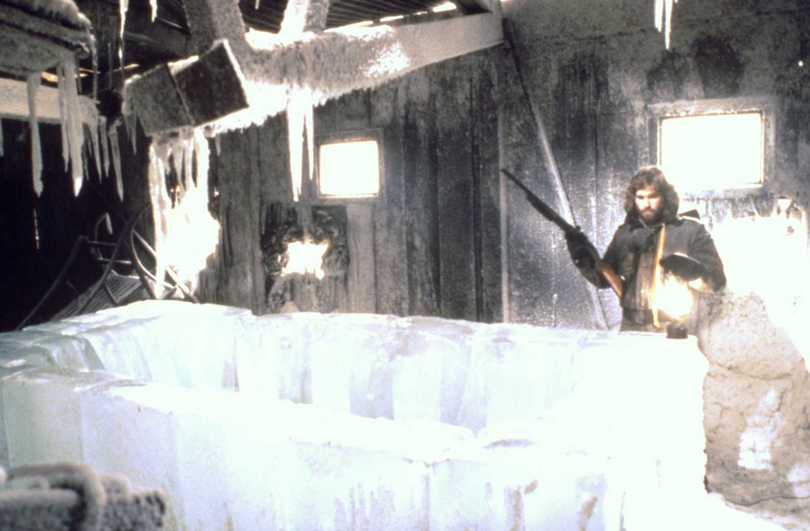 MacReady holds a rifle while looking at the Norwegian outpost in John Carpenter's The Thing