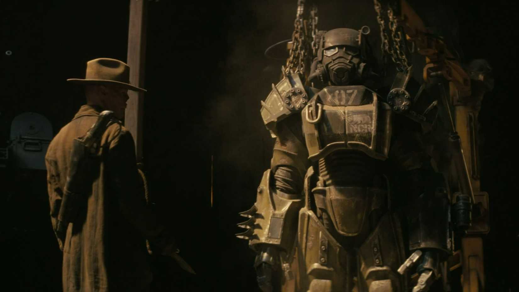 The Ghoul standing beside an NCR power armor suit in the Fallout TV show.