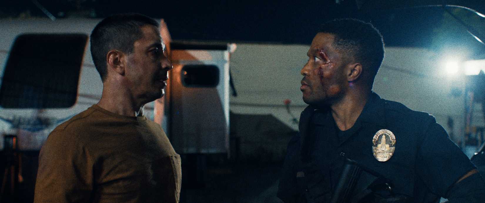 A white man and a Black cop (Justin Long and Jermaine Fowler), both battered and bloodied, face off in the dark in Night Patrol