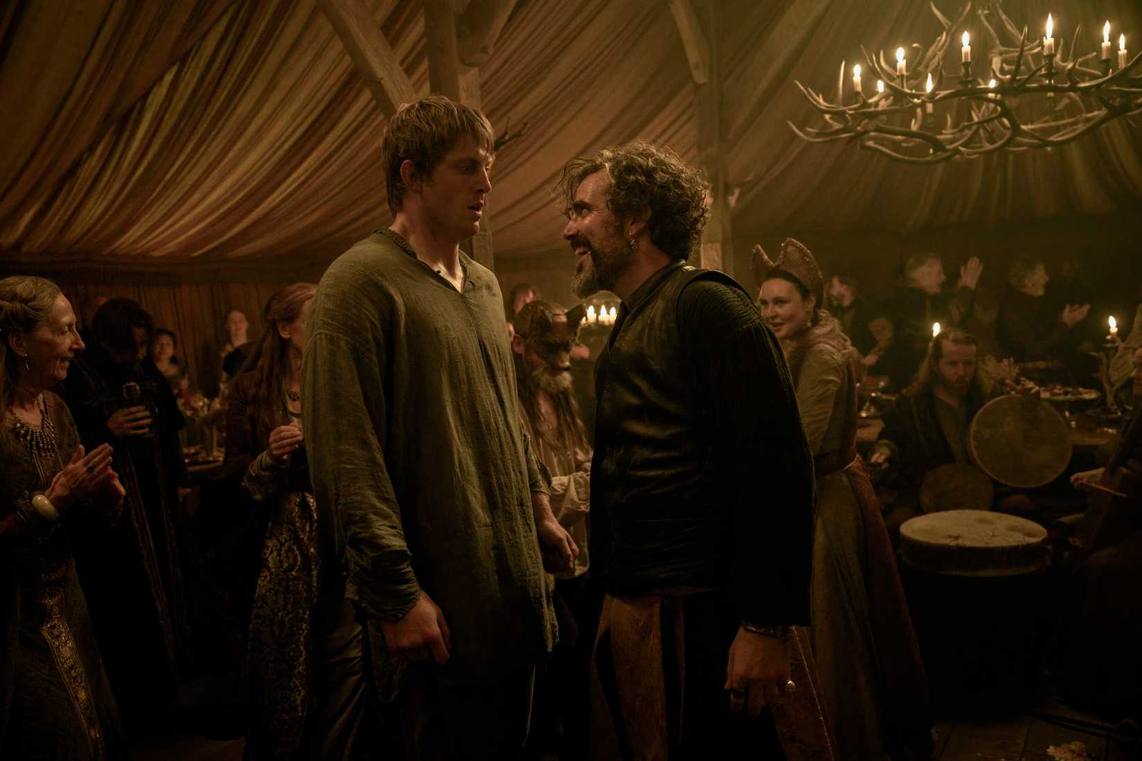 Dunk (Peter Claffey), a tall man in a loose homespun shirt, looks baffled as  Ser Lyonel Baratheon (Daniel Ings) grins at him inside a dim tent full of people in the Game of Thrones prequel A Knight of the Seven Kingdoms