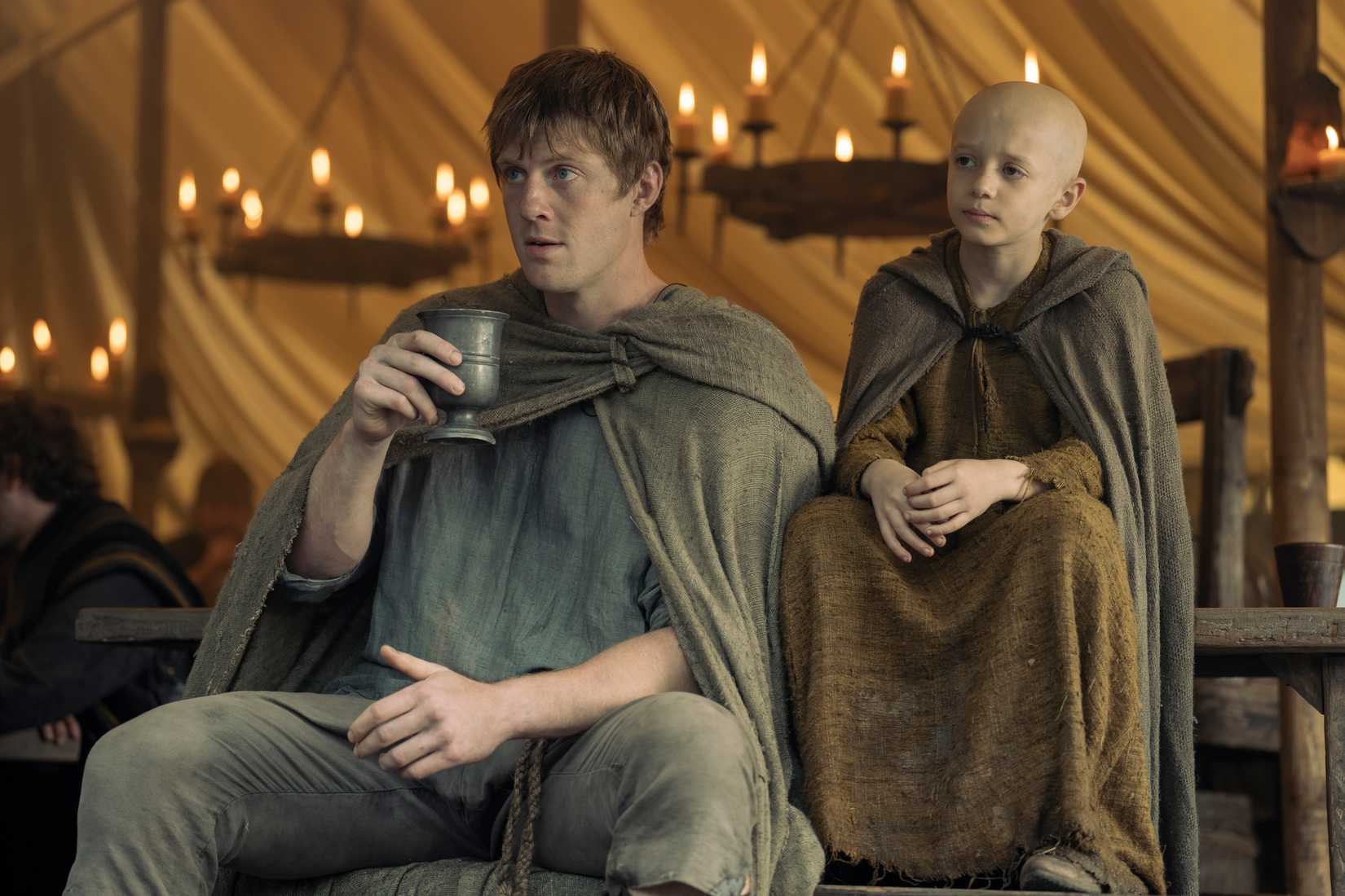 Dunk (Peter Claffey) and Egg (Dexter Sol Ansell), a tall man and a small bald boy, sit together in the Game of Thrones prequel A Knight of the Seven Kingdoms 