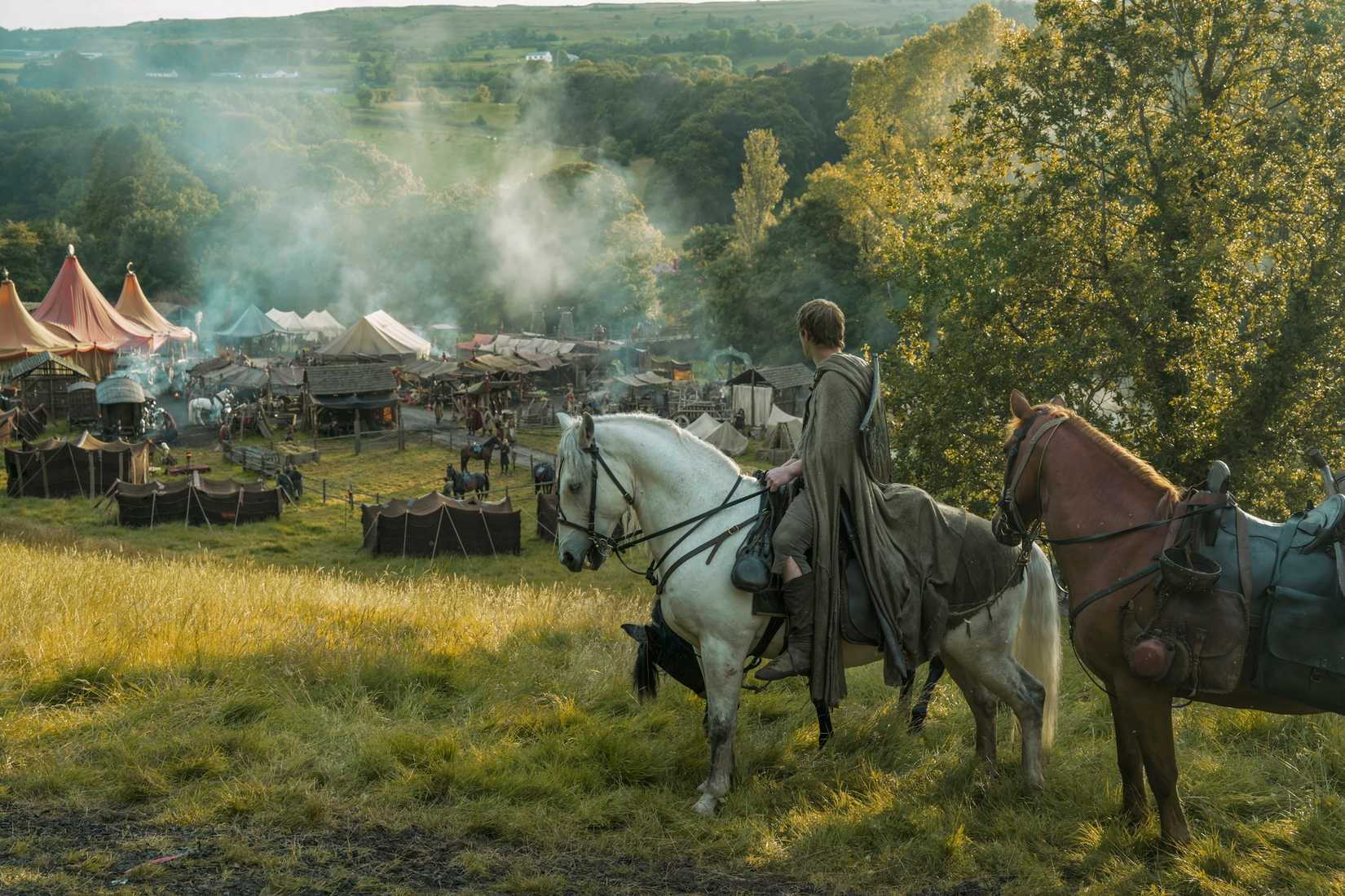 Dunk (Peter Claffey), a tall man in a long green cloak, sits on horseback on a hill above a small medieval town in the Game of Thrones spin-off A Knight of the Seven Kingdoms