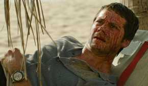 Bradley (Dylan O'Brien), a bedraggled man with a huge amount of blood spattered across his face, lies on a beach looking dumbstruck in Send Help