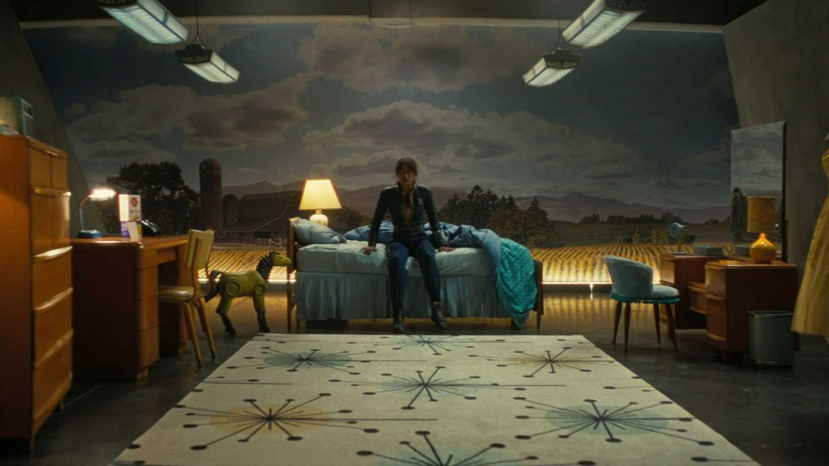 Lucy sitting on a bed in a simulation room in the Fallout TV show.