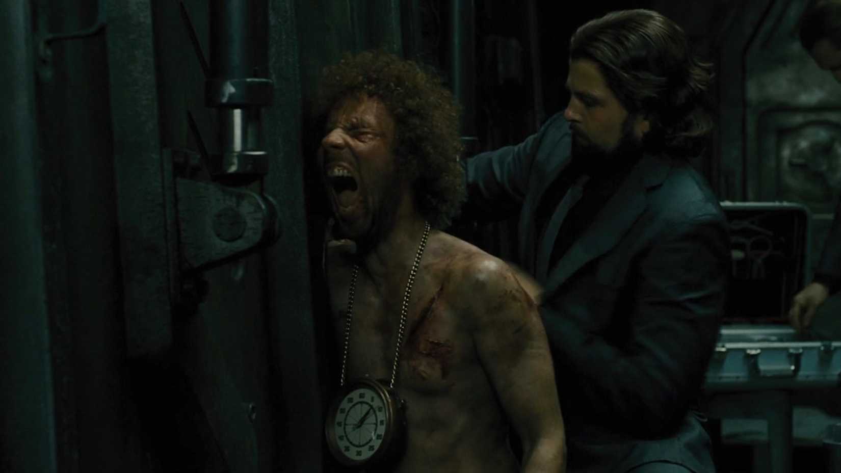 Andrew's arm is shoved through the hole in the train as he screams with a ticking clock around his neck in Snowpiercer