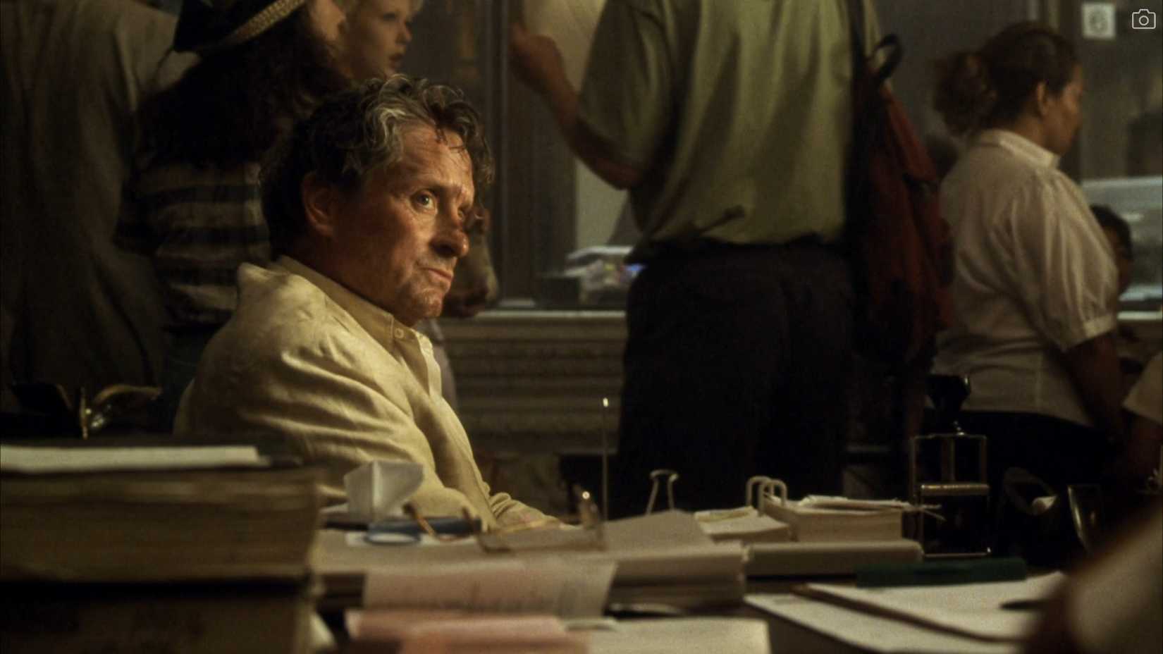 A somewhat bedraggled and dirtied-up Michael Douglas sits in a bustling police station in a scene from David Fincher's The Game