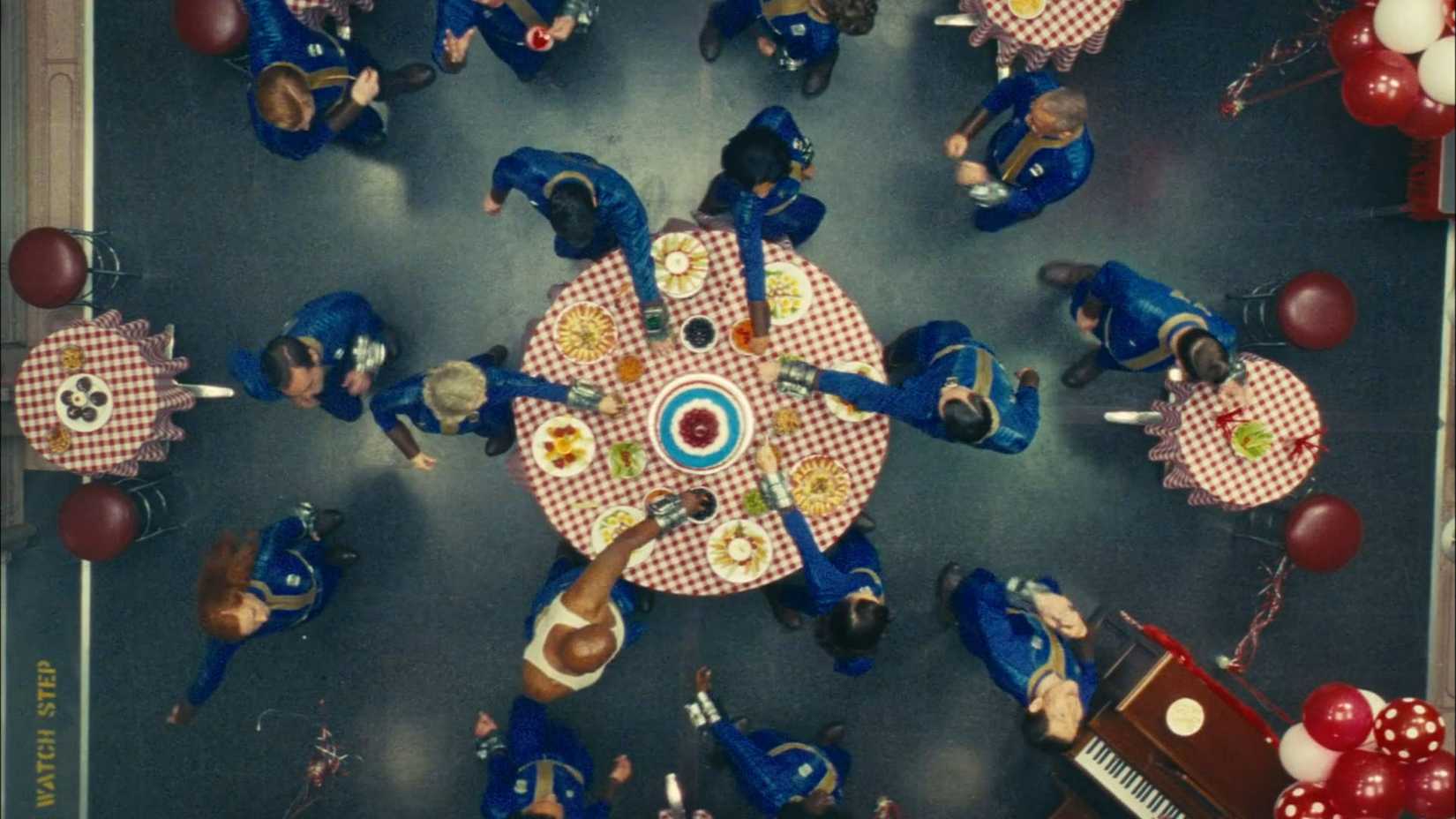Members of Vault 33 spinning around a table with food in the Fallout TV show.
