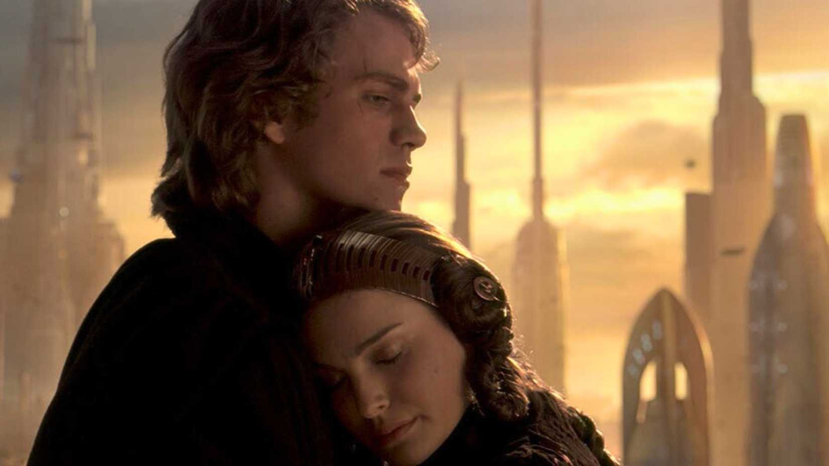 An image of Anakin Skywalker and Padme Amidala from Star Wars: Revenge of the Sith. It shows Padme, hair up and wearing a sci-fi esque headband, leaning into Anakin. Anakin had brown hair that ends above his shoulders. He has a scar on his right eye, and a pensive look on his face.