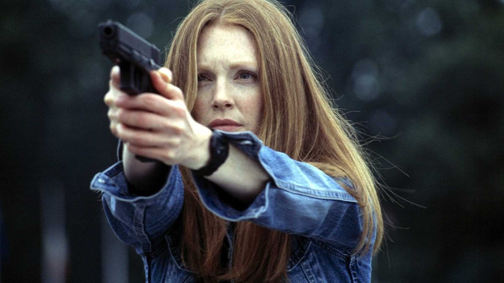 Clarice Starling (Julianne Moore) aims a gun outdoors at an offscreen target in a scene from Hannibal (2001).