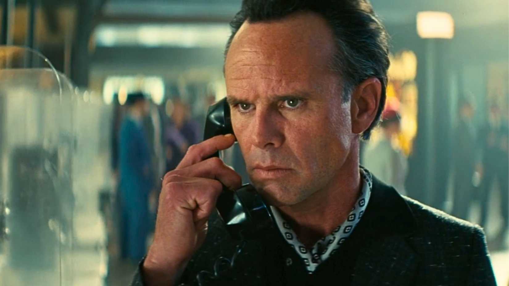 An image from Fallout season 2 featuring Walton Goggins as Cooper Howard. He has slicked back hair and wears a neckerchief. He looks worried and has a payphone pressed to his ear.