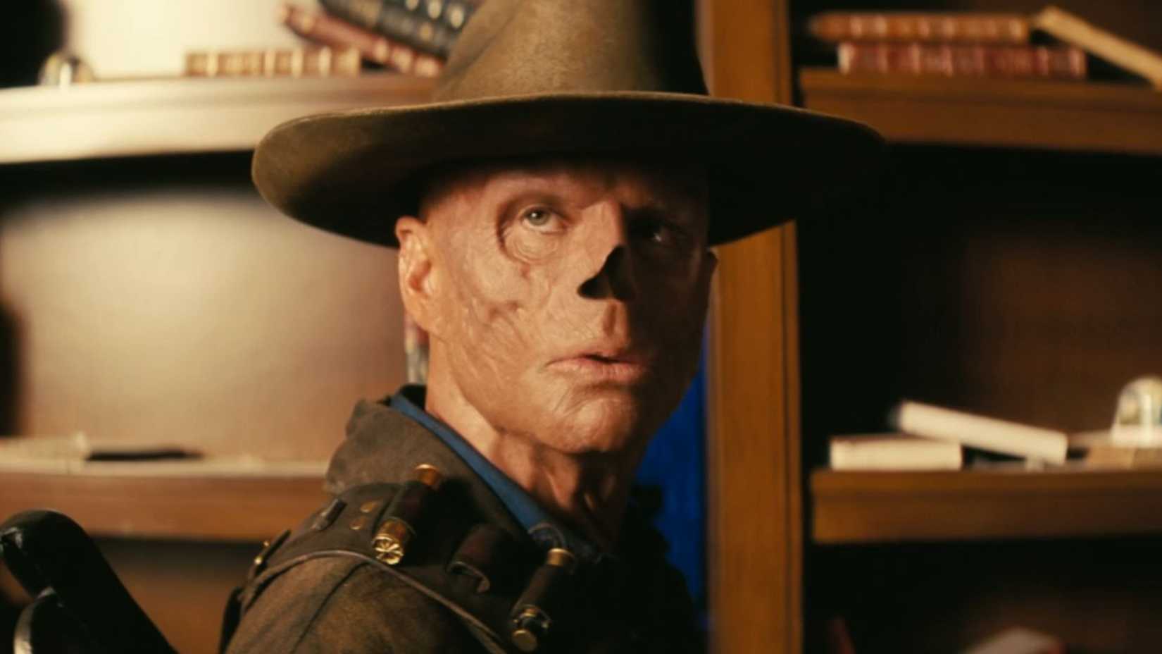 An image of Walton Goggins as the Ghoul from Fallout season 2. His skin is patchy and he has no nose. He wears a stetson hat, and a leather dust. He turns to address someone off screen, looking annoyed.